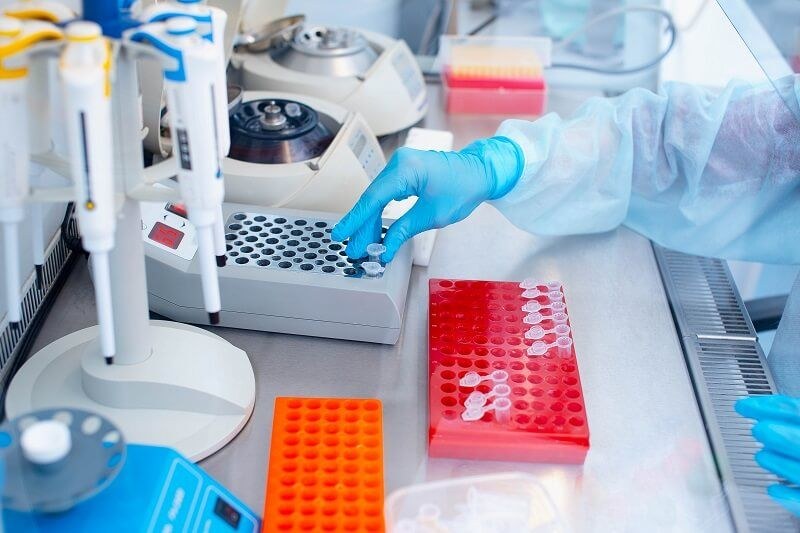 A gloved technologist loading sample tubes at a laboratory bench